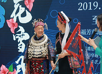 2019年8月3日，在北京侨福芳草地购物中心，苗族绣娘潘玉珍（左一）将象征脱贫希望的龙旗传递给年轻绣娘。